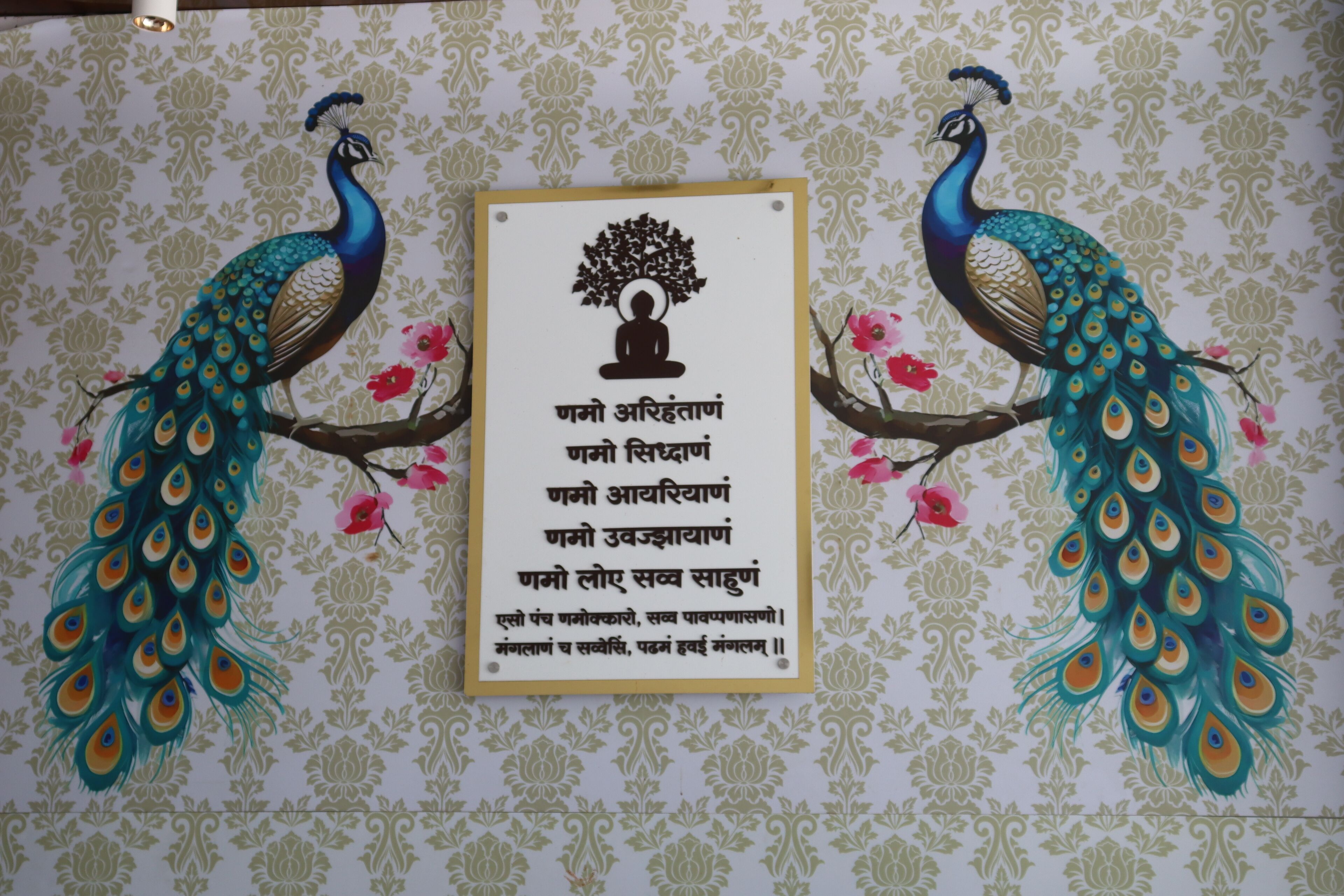 Eine Wand mit Pfau-Illustrationen und einer gerahmten Textbox mit Baum und meditierender Figur.