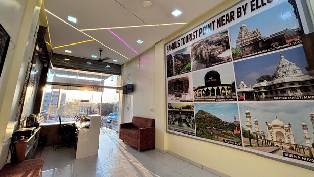 A hotel lobby with a reception desk, a sofa, a TV mounted on the wall, and a poster of famous tourist attractions. - Hotel Mayur Residency (Khuldabad)