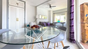 A dining area with a glass table and chairs, a sofa, and a wooden cabinet.