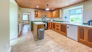 A kitchen with wooden cabinets, a white countertop, and a window with a view of greenery. - Hafod Fach - UKC6956 (Moylegrove near Ceibwr Bay)