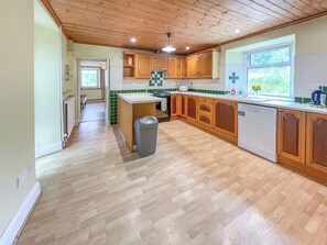 A kitchen with wooden cabinets, a white countertop, and a window with a view of greenery.