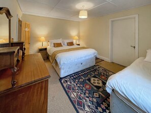 A bedroom with a bed, bedside tables, a dresser, a rug, and a door. - Hafod Fach - UKC6956 (Moylegrove near Ceibwr Bay)