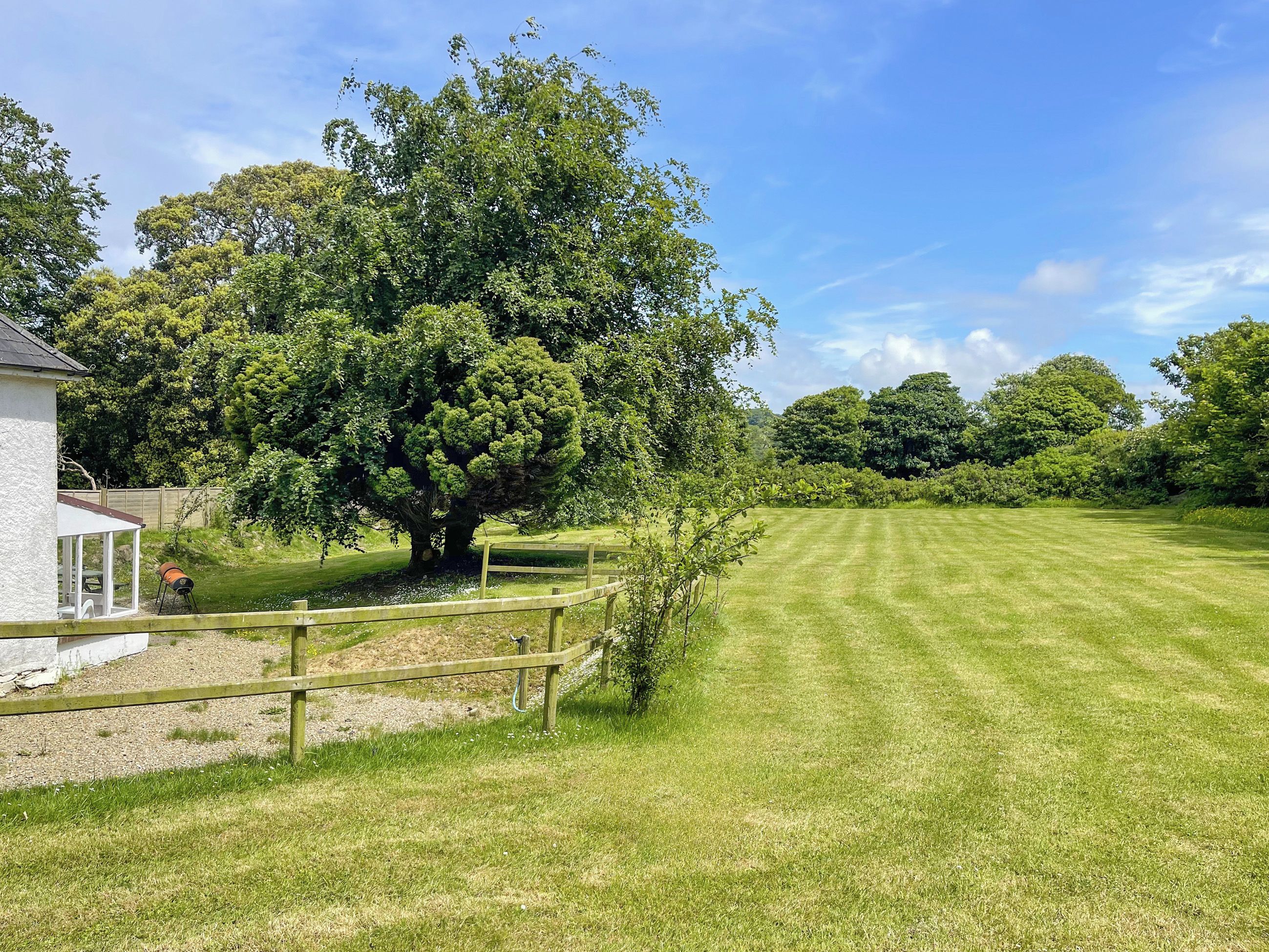 A well-maintained lawn with a large tree, a wooden fence, and a small building with a covered area.