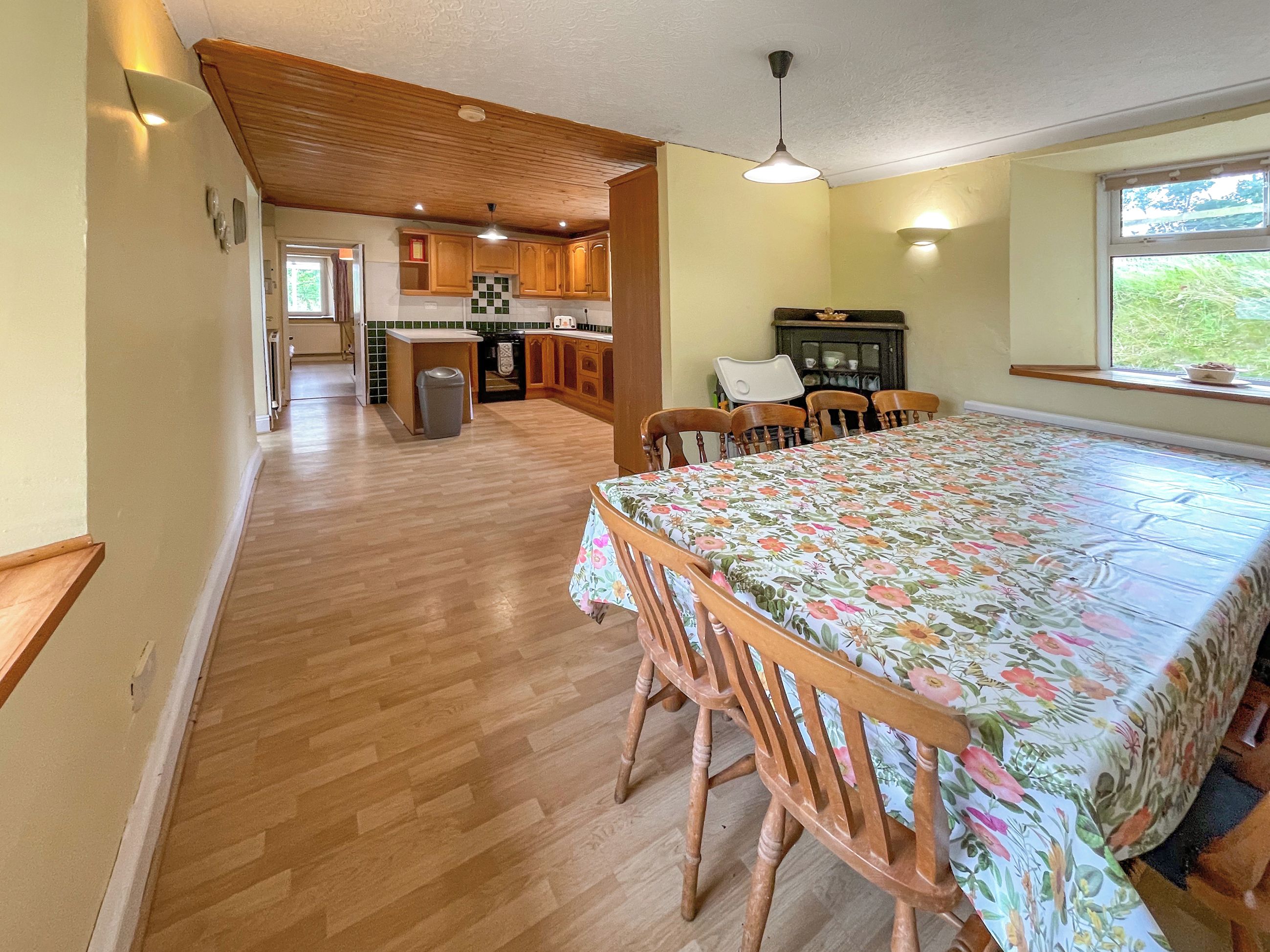 A spacious kitchen with wooden cabinets, a dining table with floral tablecloth, and a window with a view.