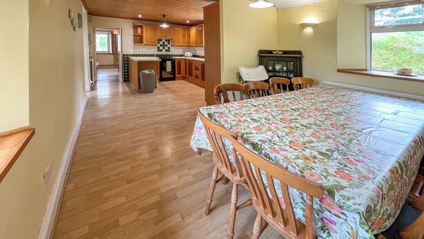 A spacious kitchen with wooden cabinets, a dining table with floral tablecloth, and a window with a view. - Hafod Fach - UKC6956 (Moylegrove near Ceibwr Bay)
