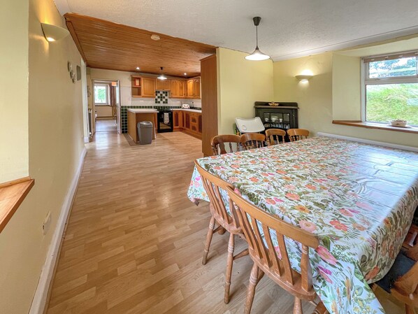 A spacious kitchen with wooden cabinets, a dining table with floral tablecloth, and a window with a view.