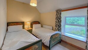 A bedroom with two single beds, a window with curtains, a hanging light fixture, and a radiator. - Hafod Fach - UKC6956 (Moylegrove near Ceibwr Bay)