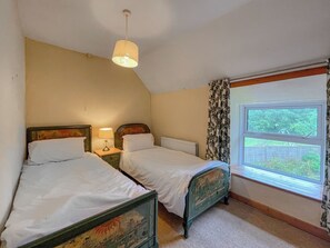 A bedroom with two single beds, a window with curtains, a hanging light fixture, and a radiator.