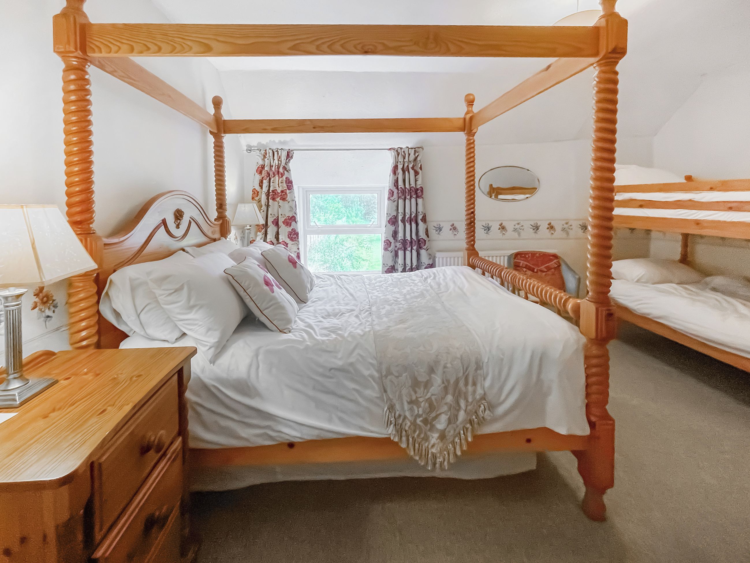 A four-poster bed with white bedding, a wooden nightstand, and a dresser.