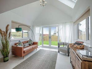 Un salon spacieux avec un canapé en cuir marron, un tapis à motifs, un meuble en bois et une vue sur le jardin, accessible par de grandes portes vitrées.