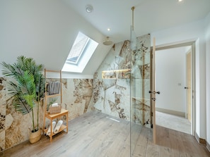 A modern bathroom with a skylight, marble walls, a glass shower enclosure, and a wooden bench with towels. - 4 bedroom accommodation in Berwick-upon-Tweed (Berwick-upon-Tweed)
