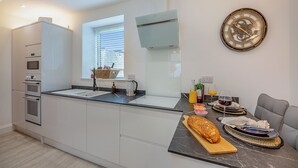 Une cuisine moderne dotée d’appareils électroménagers intégrés, un coin repas avec une table dressée pour deux personnes et une horloge murale.