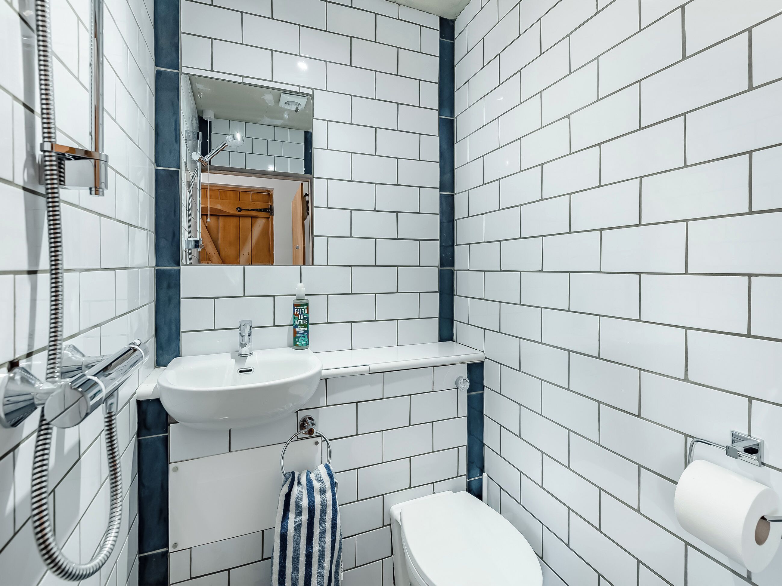 A bathroom with white tiles, a sink, a mirror, a towel rack, and a toilet.