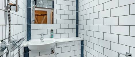 A bathroom with white tiles, a sink, a mirror, a towel rack, and a toilet.