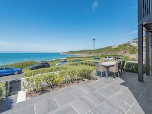 Une terrasse avec vue sur la mer, une table avec des chaises et des voitures garées.