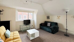 A living room with a sofa, a television on a glass stand, a green sofa, a white coffee table, and a floor lamp.