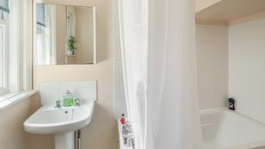 A bathroom with a sink, mirror, shower curtain, and a bathtub.