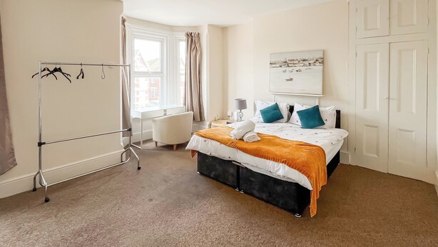 A hotel room with a bed, a desk, a chair, a coat rack, and a window with curtains.
