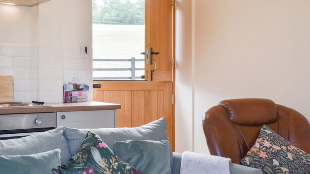 A cozy living area with a sofa, a brown leather chair, and a window with a view of trees. - Pheasant Pens 1 - UK50187 (Llandenny, near Usk)