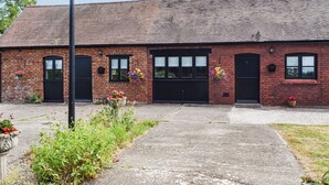 A brick building with two black doors and windows, a concrete pathway, and flower planters. - Pheasant Pens 1 - UK50187 (Llandenny, near Usk)
