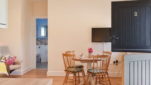 A modern living room with a wooden dining table, four chairs, a sofa, and a TV mounted on the wall. - Pheasant Pens 2 - UK50188 (Llandenny, near Usk)