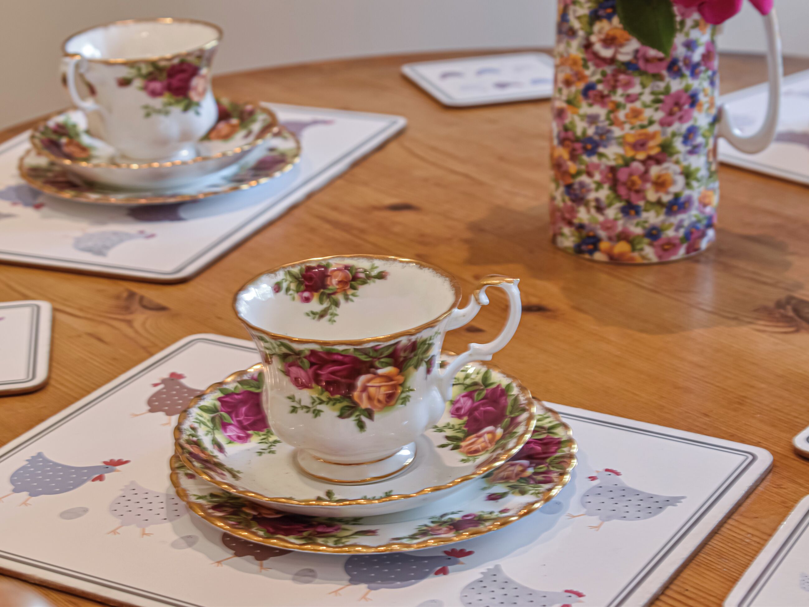 A table with a floral-patterned teapot, a matching teacup and saucer, and matching coasters.