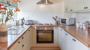 A modern kitchen with white cabinets, a stainless steel range hood, a built-in oven, a microwave, and a kettle. - Pheasant Pens 2 - UK50188 (Llandenny, near Usk)