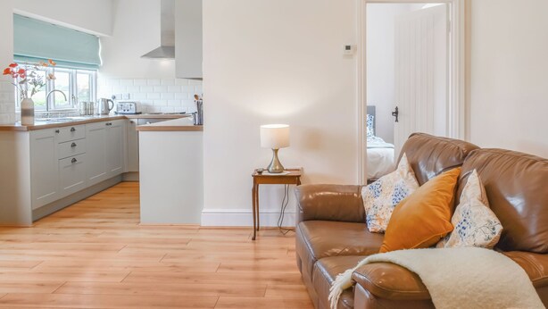 A modern kitchen with white cabinets and a wooden countertop, a brown leather sofa with cushions, and a small table with a lamp. - Pheasant Pens 2 - UK50188 (Llandenny, near Usk)