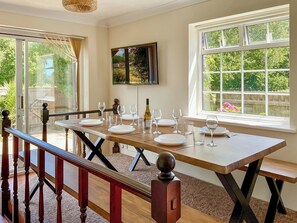 A dining area with a table set for six, large windows, and a view of greenery outside. - 4 bedroom accommodation in Poole (Poole)