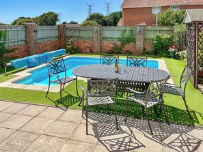 A backyard with a swimming pool, a patio table with chairs, and a brick wall. - 4 bedroom accommodation in Poole (Poole)