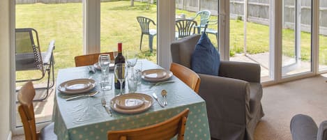 A dining area with a table set for four, chairs, and a view of the backyard through large windows.