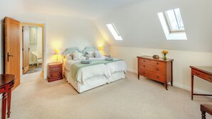 A bedroom with a bed, bedside tables, a dresser, a desk, and a skylight.