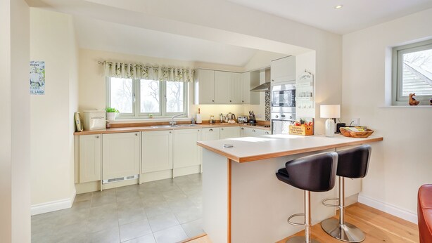 A modern kitchen with white cabinets, a central island with bar stools, a built-in oven, and a window with a view.