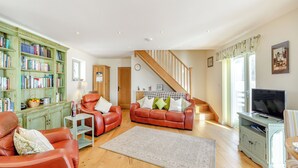 A spacious living room with leather sofas, a bookshelf, a television, and a staircase.