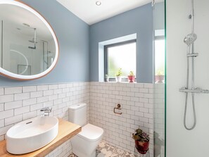 A bathroom with a round mirror, two sinks, a toilet, and a shower.