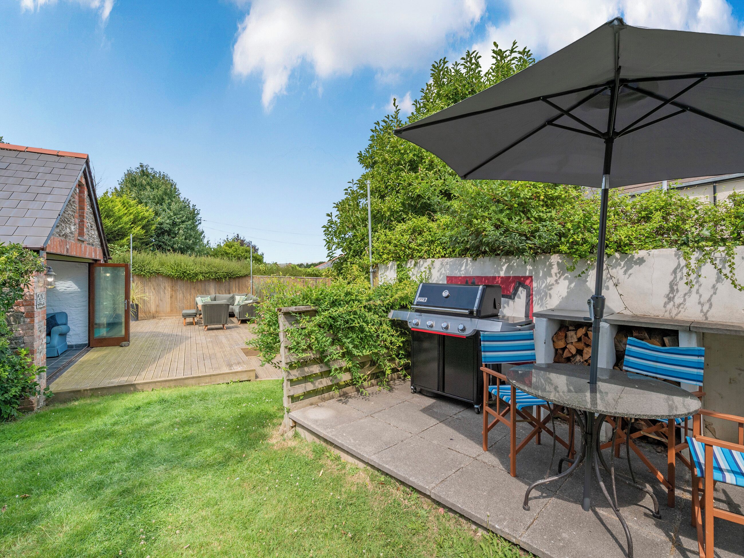 A backyard with a barbecue area, a wooden deck, and a patio with outdoor furniture.