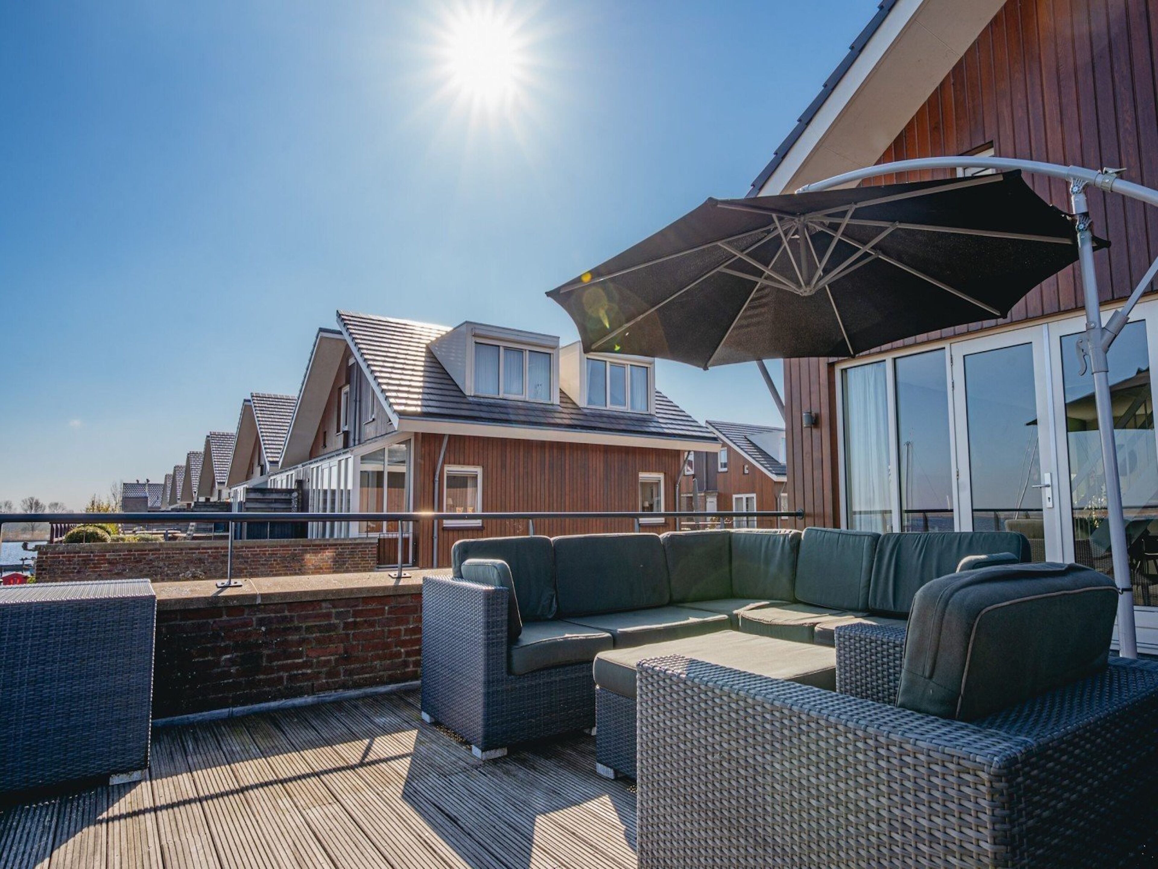 A deck with outdoor furniture and a large umbrella, overlooking a residential area with modern houses.