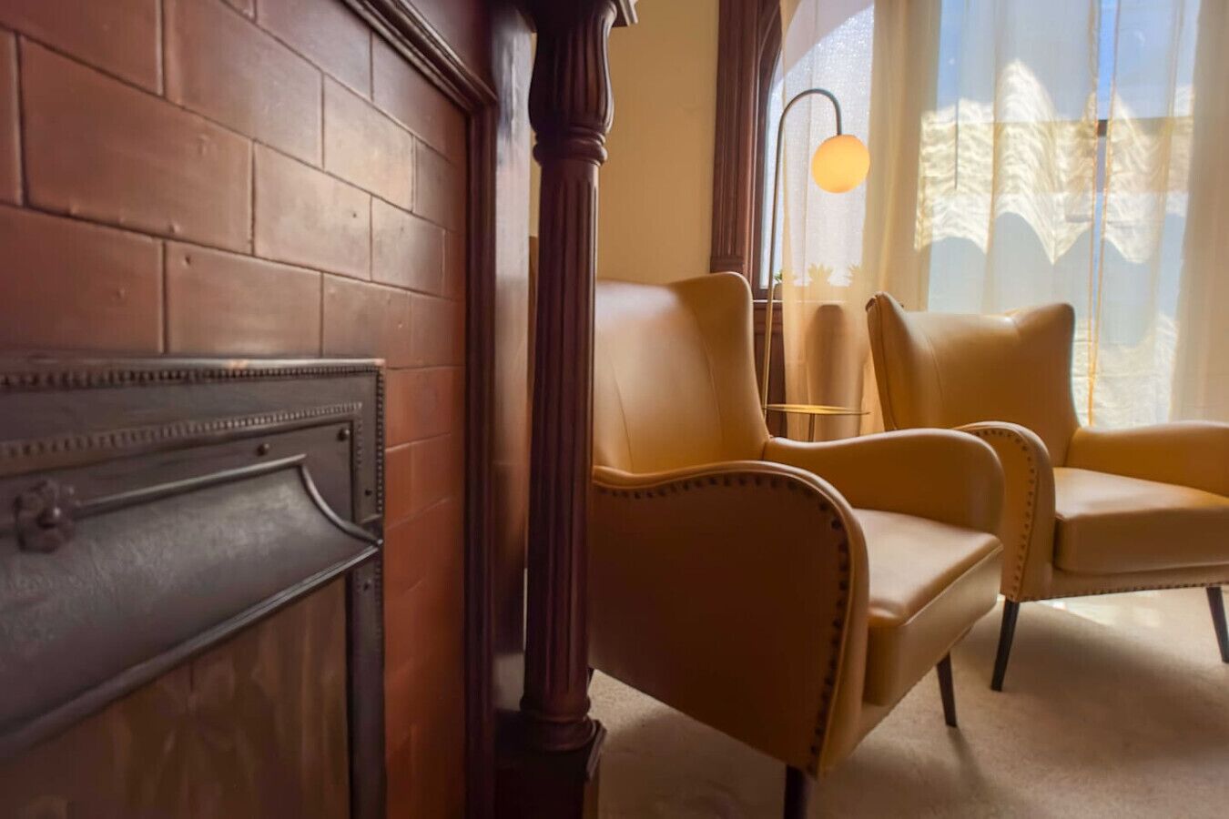 Una habitación con chimenea, sillones de cuero y un gran ventanal con cortinas translúcidas.