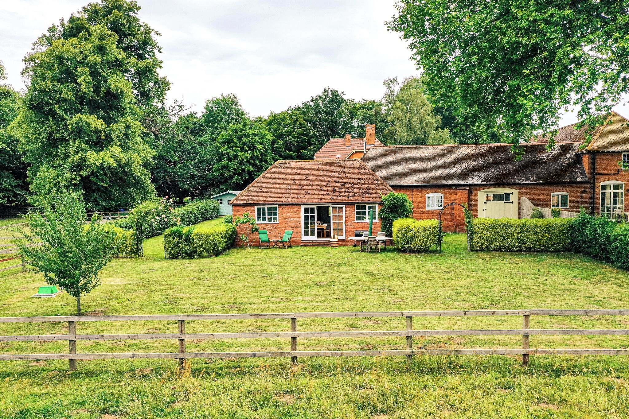 A traditional brick house with a well-maintained lawn, a wooden fence, and a small patio area with outdoor seating.