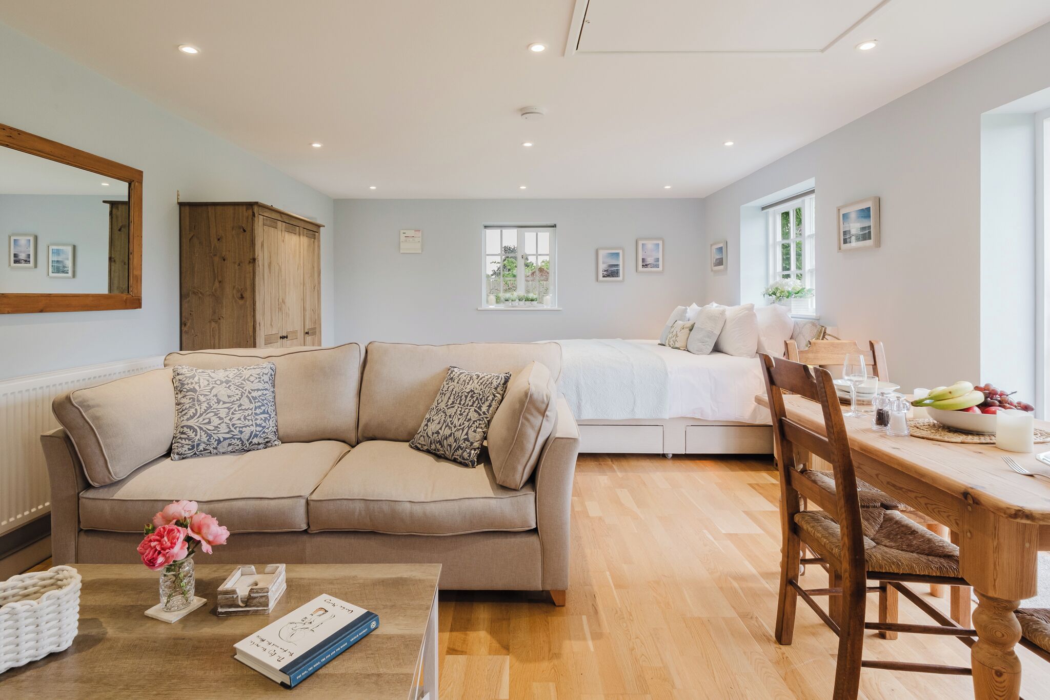 Ein gemütliches Wohnzimmer mit einem beigen Sofa, einem Holzessttisch und einem weißen Esstisch für vier Personen.