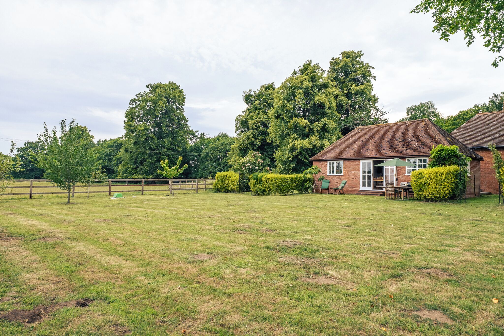 A grassy field with a brick house, a wooden fence, and a large tree.