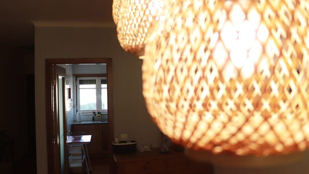 A room with a wicker lamp, a wooden cabinet, and a view of a kitchen area through an open doorway.