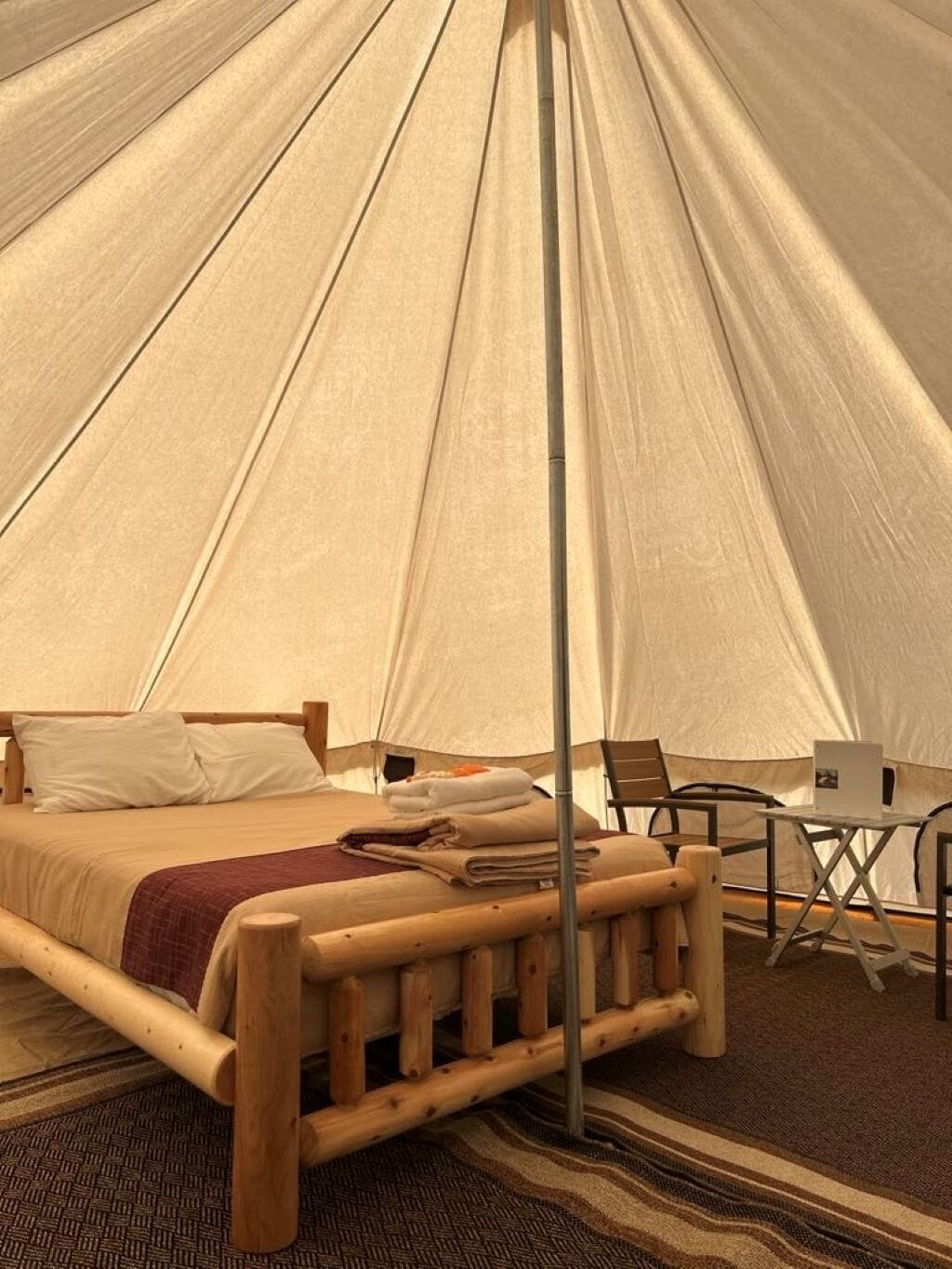 A tent with a bed, wooden furniture, and a laptop on a table.