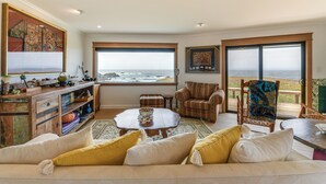 Ein gemütliches Wohnzimmer mit großem Fenster und Meerblick, einem Holztisch und bequemen Sitzgelegenheiten.