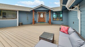Eine überdachte Terrasse mit Holzboden, ein graues Sofa mit einem roten Kissen und ein kleiner Tisch.