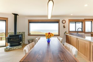 Et spiseområde med et træbord, stole, en vase med blomster, en pejs og udsigt til havet.