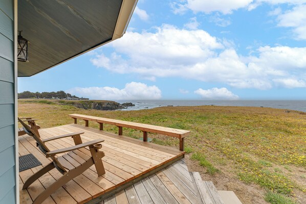 En træterrasse med bænke, med udsigt over en græsplæne og havet.