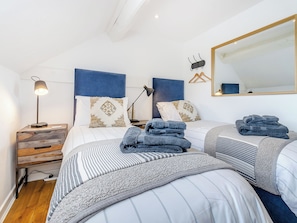 A hotel room with two beds, a nightstand, a lamp, a mirror, and a folded towel on the bed.