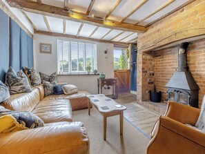A cozy living room with a leather sofa, a wooden coffee table, and a brick fireplace. - 4 bedroom accommodation in Welshpool (Welshpool)