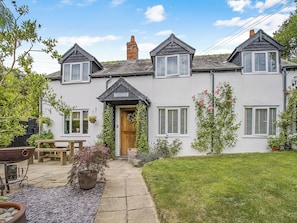 A two-story house with a front porch, a wooden bench, and a garden with potted plants. - 4 bedroom accommodation in Welshpool (Welshpool)